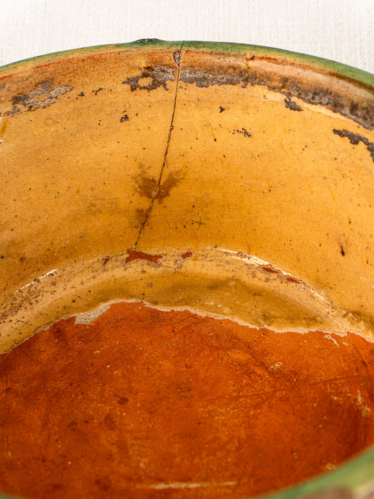 Antique French Tian bowl in Provencal terracotta with green and yellow glaze, visible stains, and side crack.