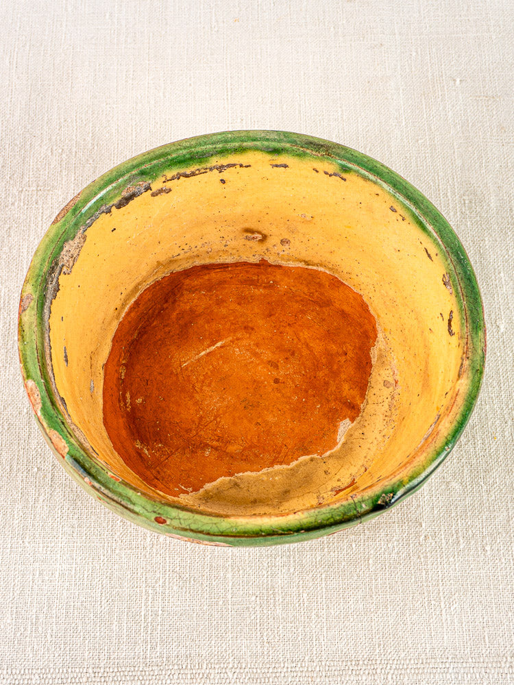 Antique French Tian bowl with yellow glazed interior and green rim on beige textured fabric.