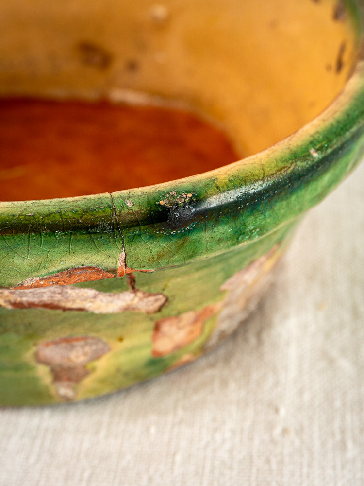 Antique French Tian Bowl in Provencal terracotta with green-yellow glaze, worn edges, on beige fabric.
