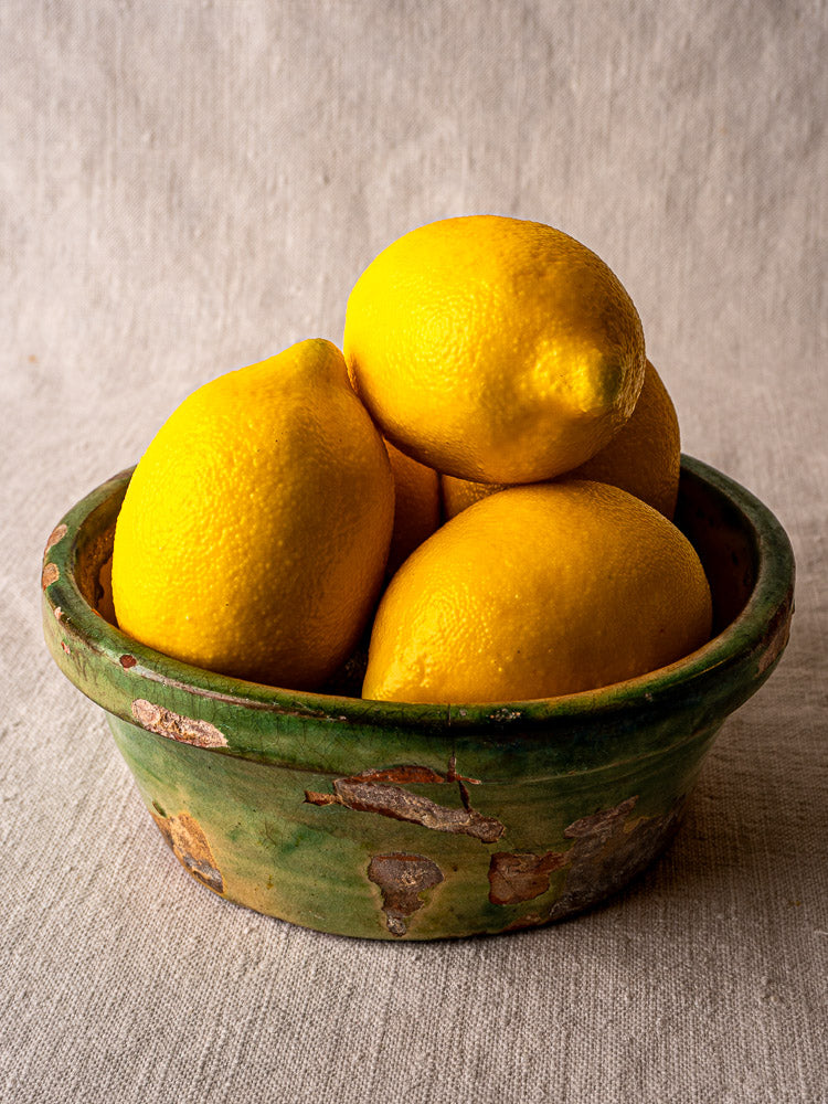 Antique French Tian bowl in Provencal terracotta with rustic green and yellow glaze, holding lemons.