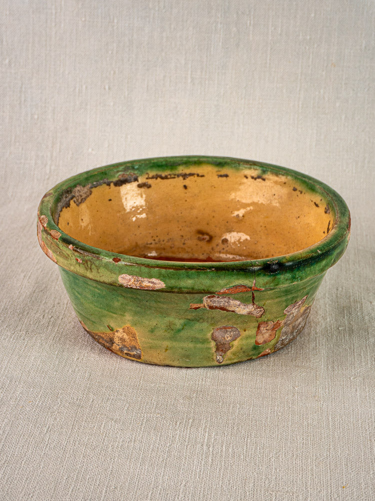 Antique French Tian bowl in Provençal terracotta with green and yellow glaze on beige textured surface.