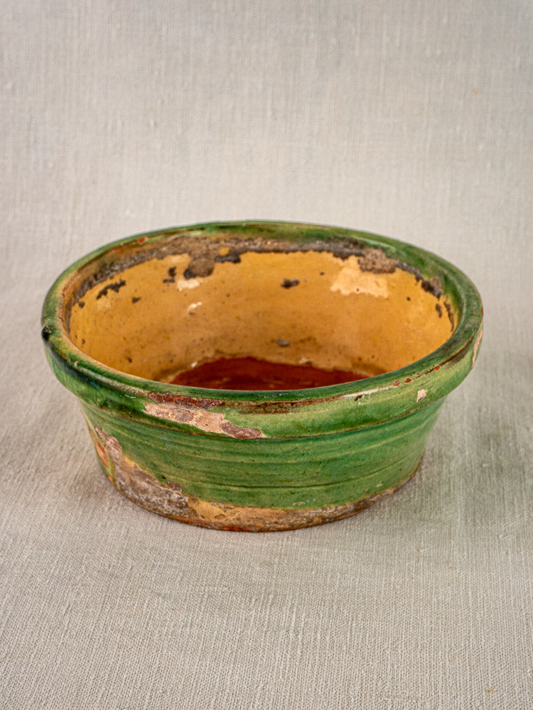 Antique French Tian bowl in Provençal terracotta with green and yellow glaze, aged patina on neutral textured surface.