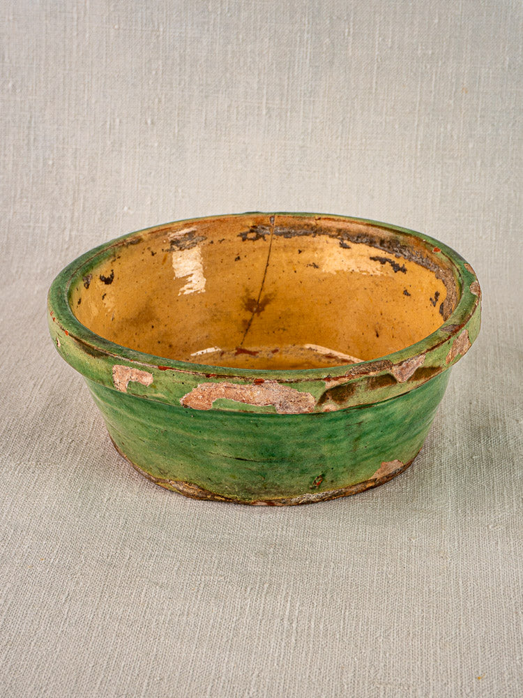 Antique French terracotta Tian bowl with rustic yellow interior and chipped green glaze, on beige surface.