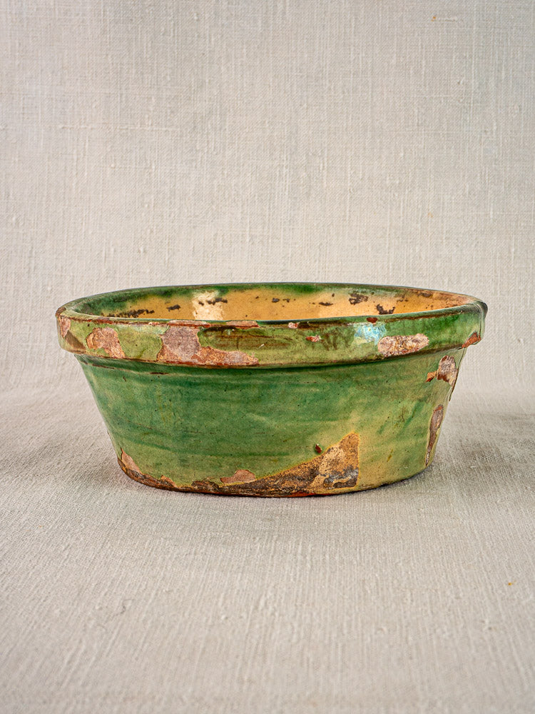 Antique French Tian bowl with green and yellow glaze, weathered terracotta finish, on neutral fabric.