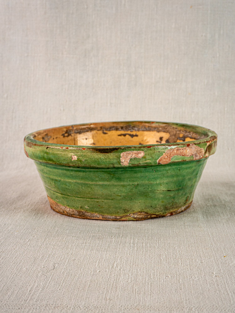 Antique French terracotta Tian bowl with green and yellow glaze, exposed clay, on fabric background.