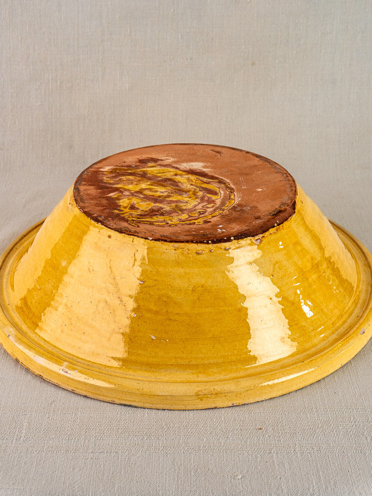 Antique French yellow glazed Provençal terracotta tian bowl, glossy ochre glaze, unglazed base, on light fabric.