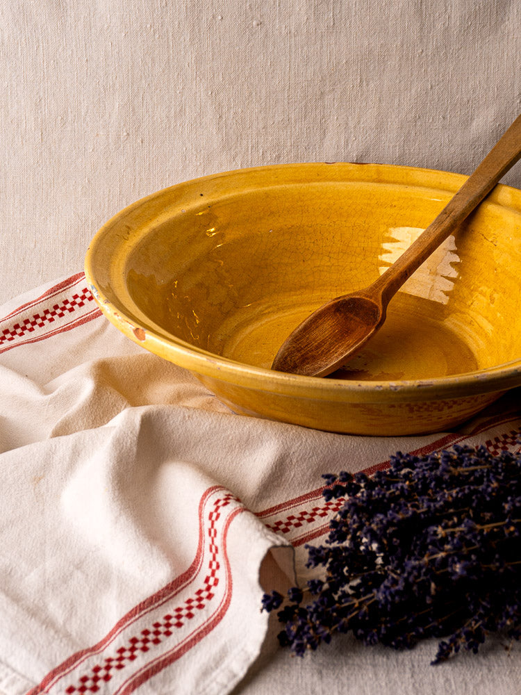 Antique French yellow glazed terracotta Tian bowl with wooden spoon, on embroidered white cloth and dried lavender.