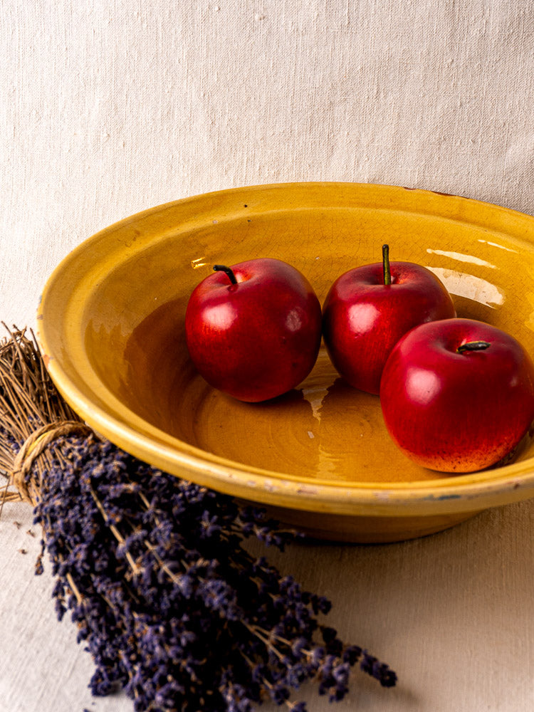 Antique French yellow glazed Tian bowl with three red apples and dried lavender on fabric.