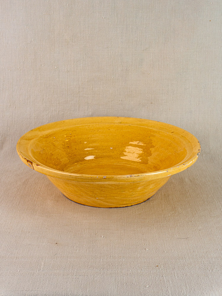 Antique French yellow glazed terracotta Tian bowl with wide rim on neutral fabric background.