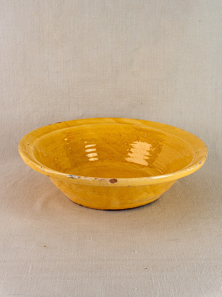 Antique French yellow-glazed Provençal terracotta Tian bowl with worn rim on beige fabric.