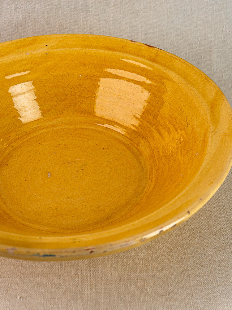 Antique French yellow glazed tian bowl with crackle finish and subtle rim imperfections on beige surface.