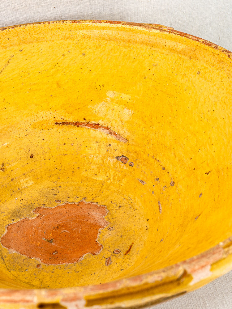 Large Provençal yellow tian bowl with rustic wear, chips, and exposed reddish clay beneath glaze.