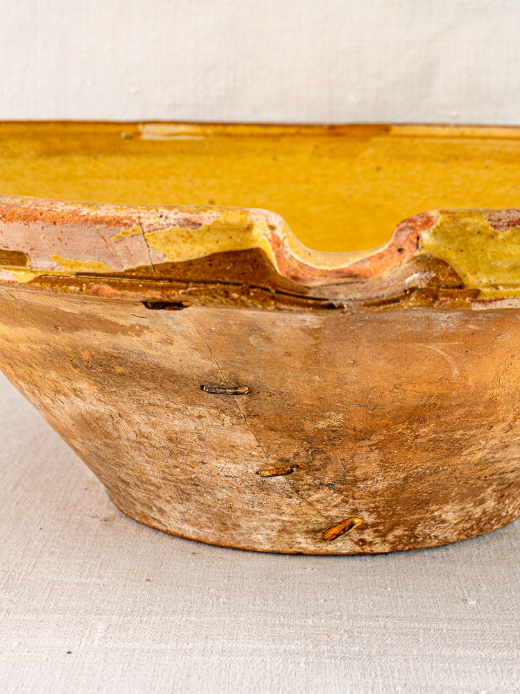 Antique Provençal terracotta bowl with saffron-yellow glazed interior and staple-repaired exterior cracks.