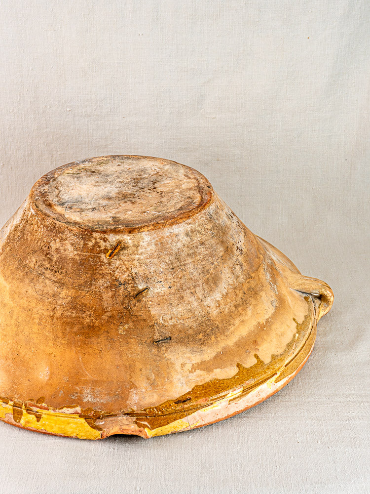 Antique Provençal yellow Tian bowl, terracotta with visible cracks, upside-down on light fabric.