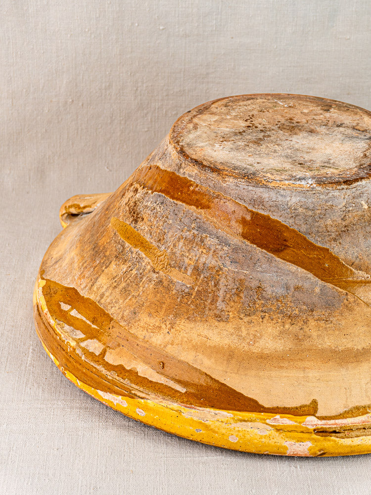 Upside-down Provençal yellow tian bowl with worn glaze in brown and saffron tones on fabric.