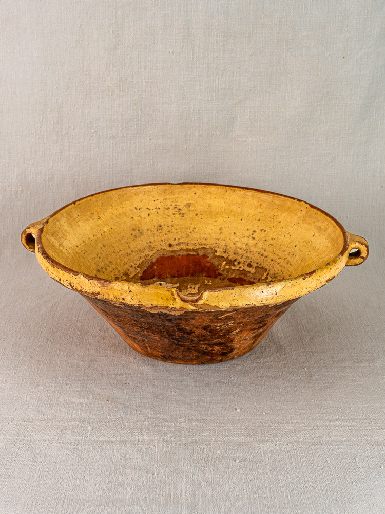 Rustic Provençal yellow tian bowl with saffron-yellow glazed interior and earthy brown exterior, on neutral fabric.
