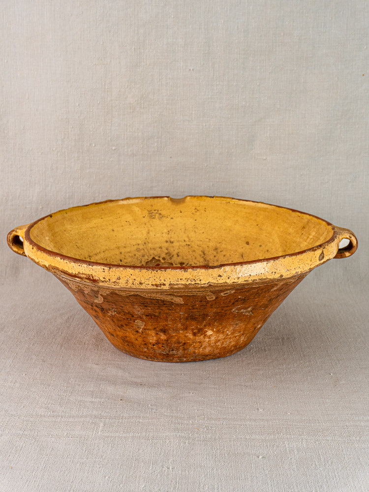 Provençal yellow ceramic tian bowls with saffron-glazed interiors, side handles, on neutral fabric background.