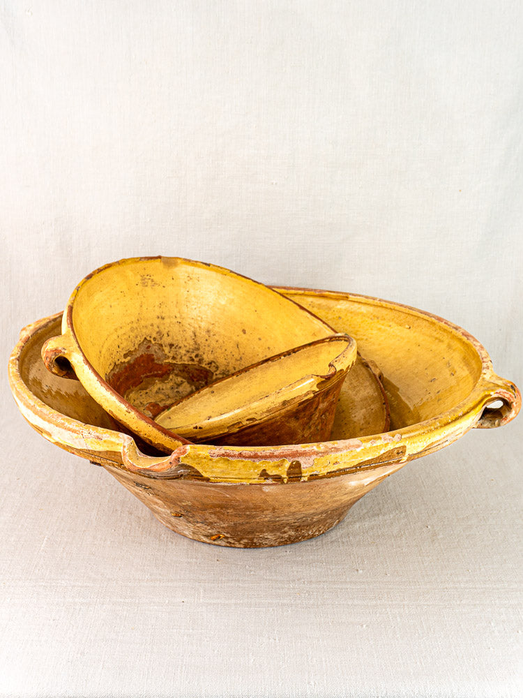 Antique Provençal yellow terracotta Tian bowls, rustic French pottery with handles and aged patina, on fabric.