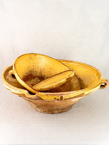 Antique Provençal yellow terracotta Tian bowls, rustic French pottery with handles and aged patina, on fabric.