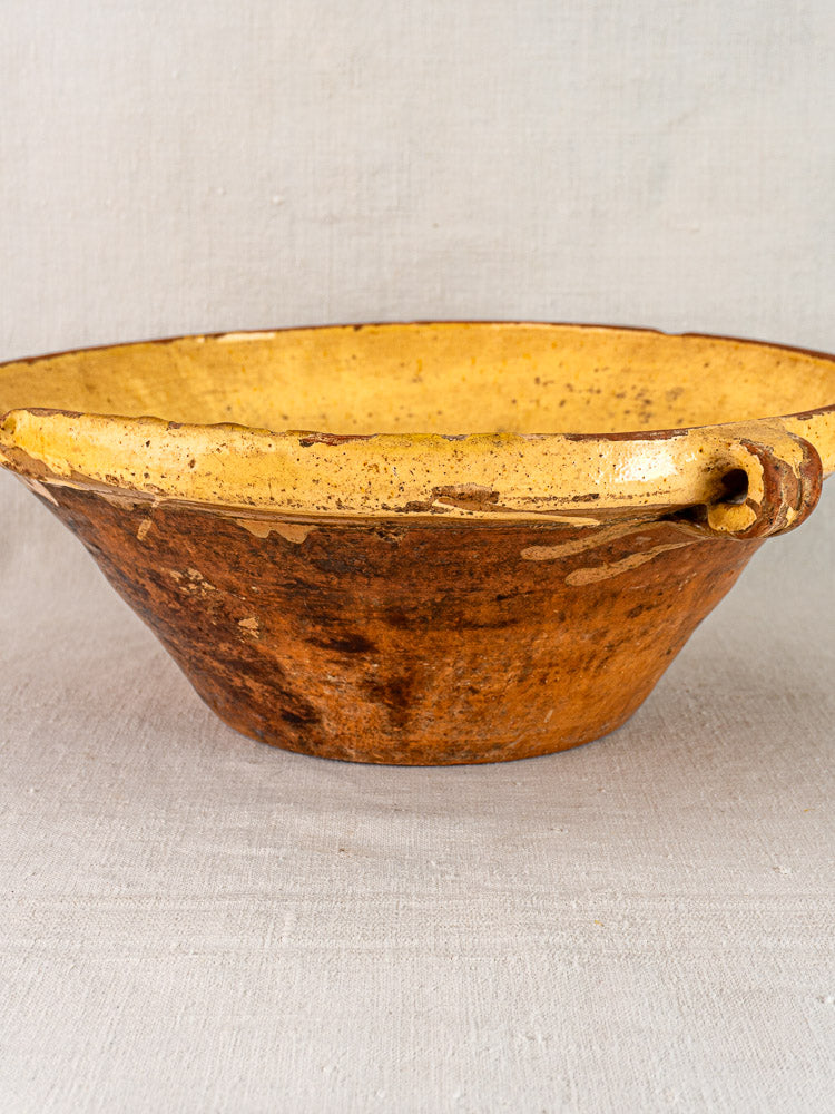 Provençal yellow tian bowl with saffron glaze, brown terracotta exterior, spout, on neutral fabric.