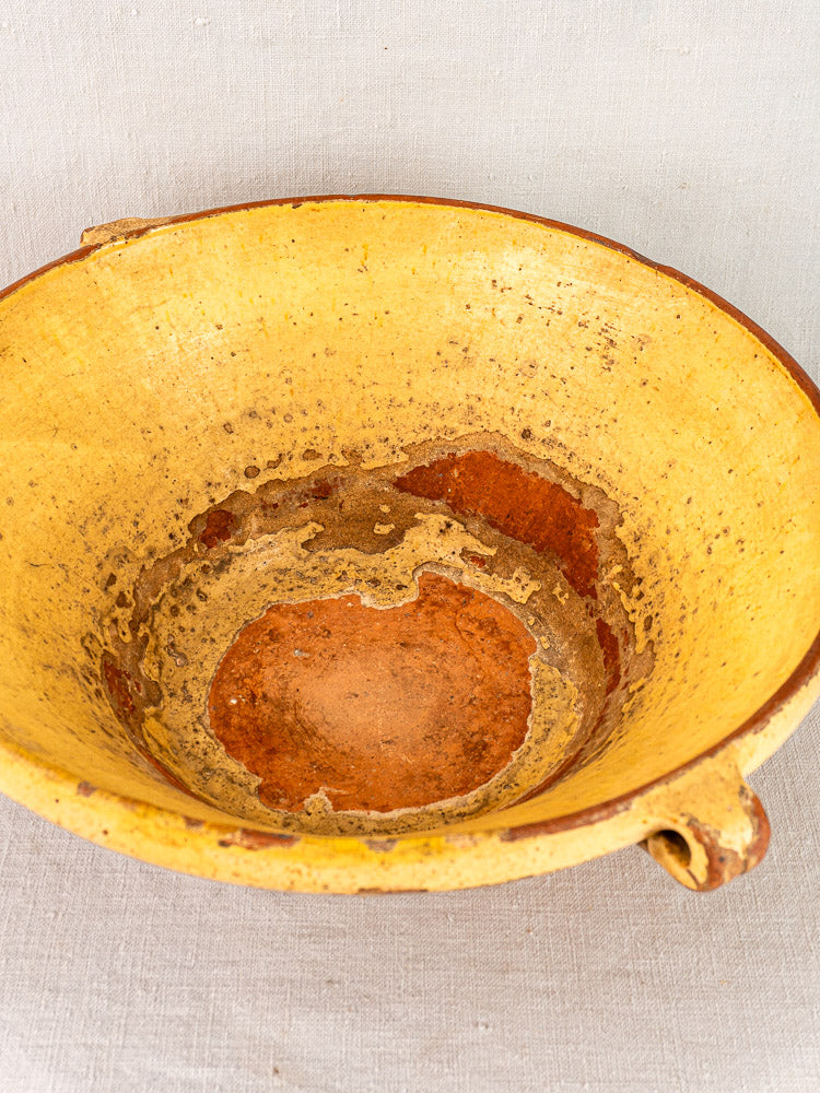 Large Provençal yellow tian bowl with saffron glaze, rustic interior, and small handle on light fabric.
