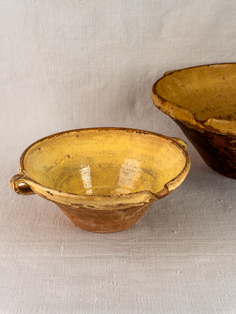 Antique terracotta Provençal yellow tian nesting bowls with saffron glaze, set on light fabric.
