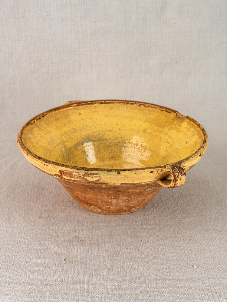 Provençal yellow tian ceramic nesting bowls with unglazed terracotta exteriors and side handles on fabric.