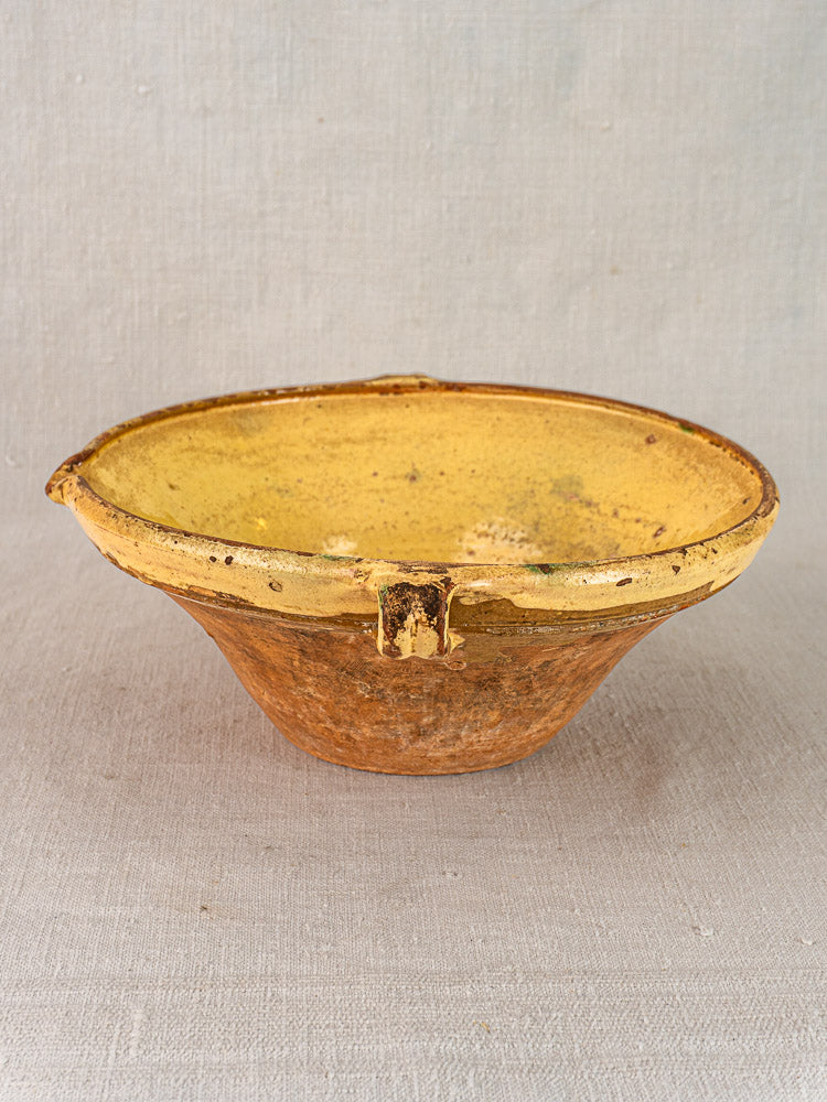 Round yellow and brown Provençal tian bowl with worn saffron glaze and textured patina on neutral fabric.