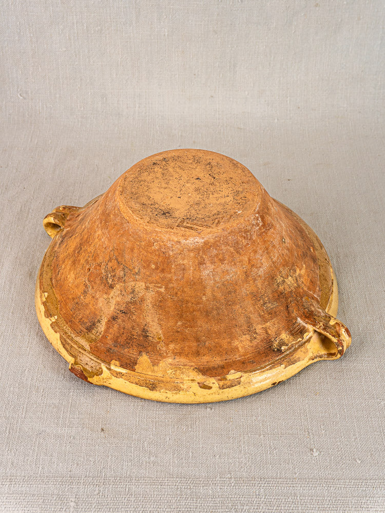 Large round Provence yellow terracotta Tian bowl upside down, flat base and curved side handles visible.