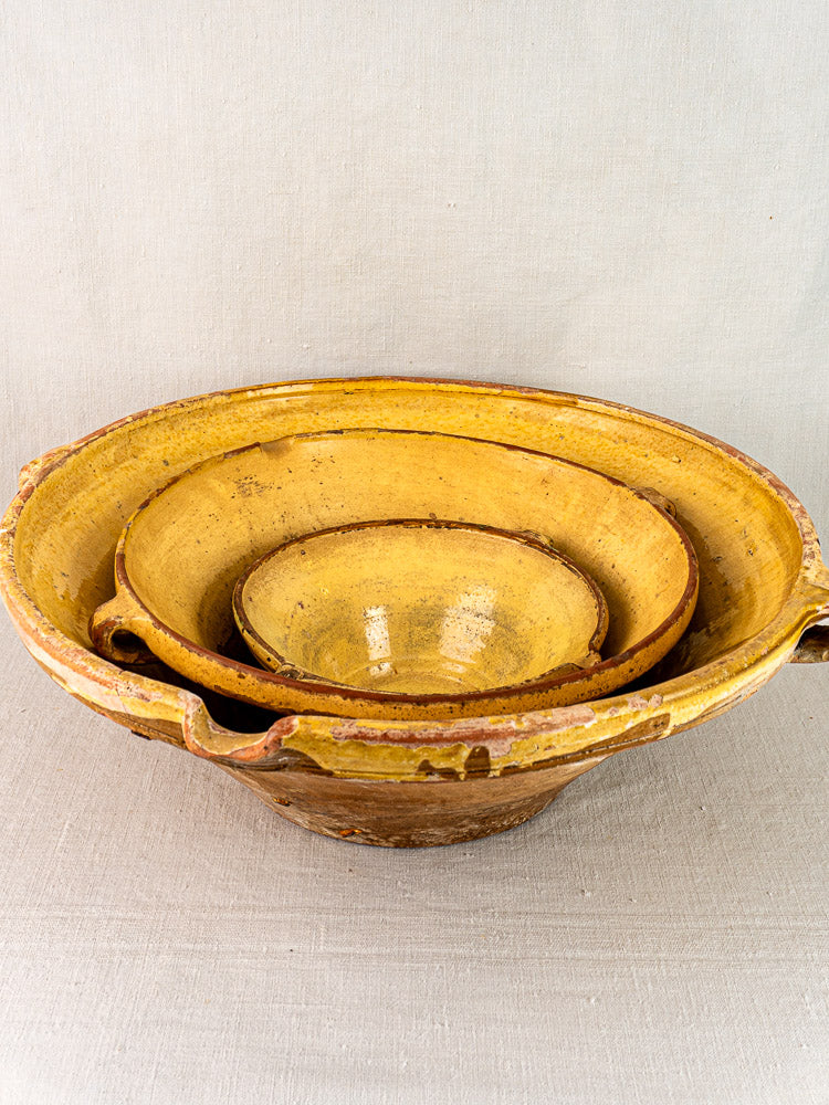 Antique Provençal yellow Tian bowls, terracotta nesting set of three, on textured light fabric.
