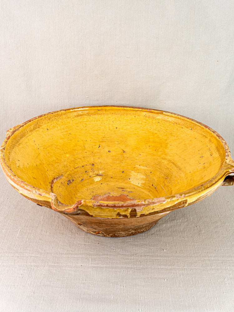 Provençal yellow glazed terra cotta tian bowl with shallow form, brown unglazed exterior on light fabric.