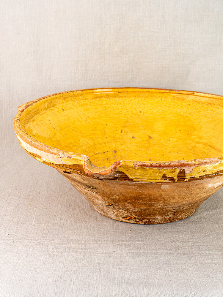 Provençal yellow tian bowl with glazed interior, textured brown exterior, and chipped antique rim on fabric.