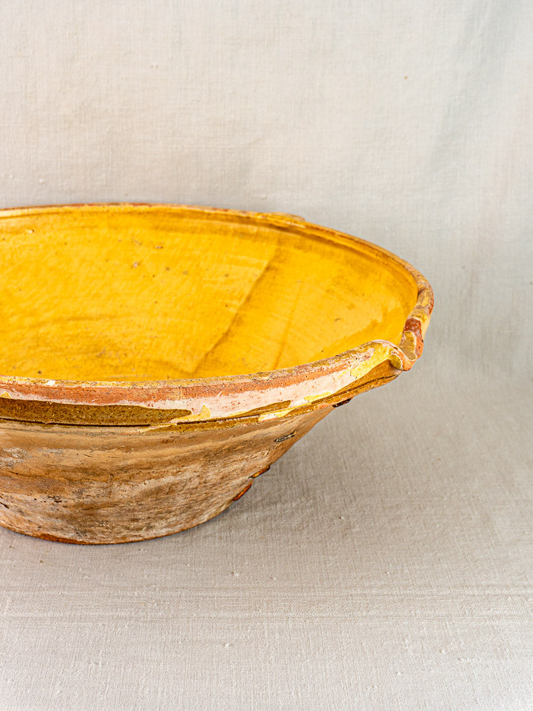 Shallow Provençal tian bowls with saffron-yellow glazed interiors, unglazed weathered exteriors, on textured fabric.