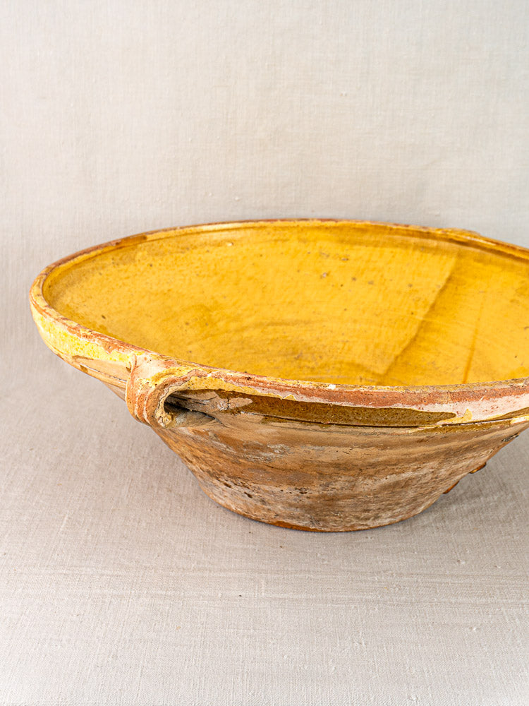 Provençal yellow tian bowl with saffron-glazed interior and weathered terracotta exterior on fabric surface.