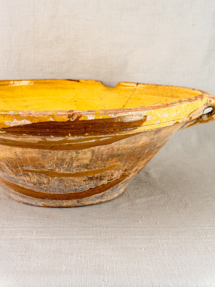 Antique Provençal yellow tian bowl with saffron glaze, brown exterior, small handle, and rim chips on fabric.