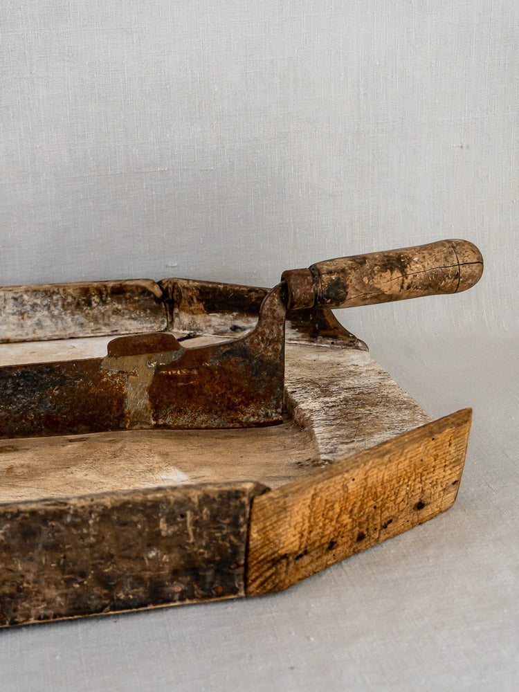 Antique French wood and iron tobacco cutter with curved blade and wooden handle on neutral background.