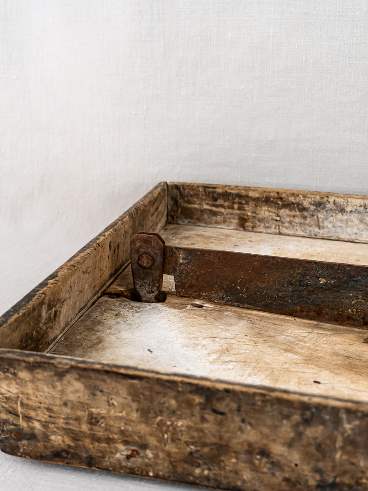French antique wood and iron tobacco cutter with rustic metal handle on a light fabric backdrop.