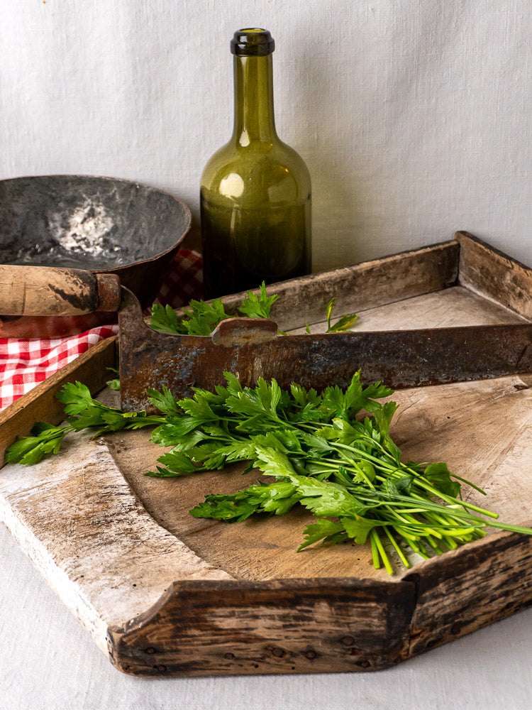 French Coupe-Tabac antique wood and iron tobacco cutter on rustic tray with green glass bottle and red checkered cloth.