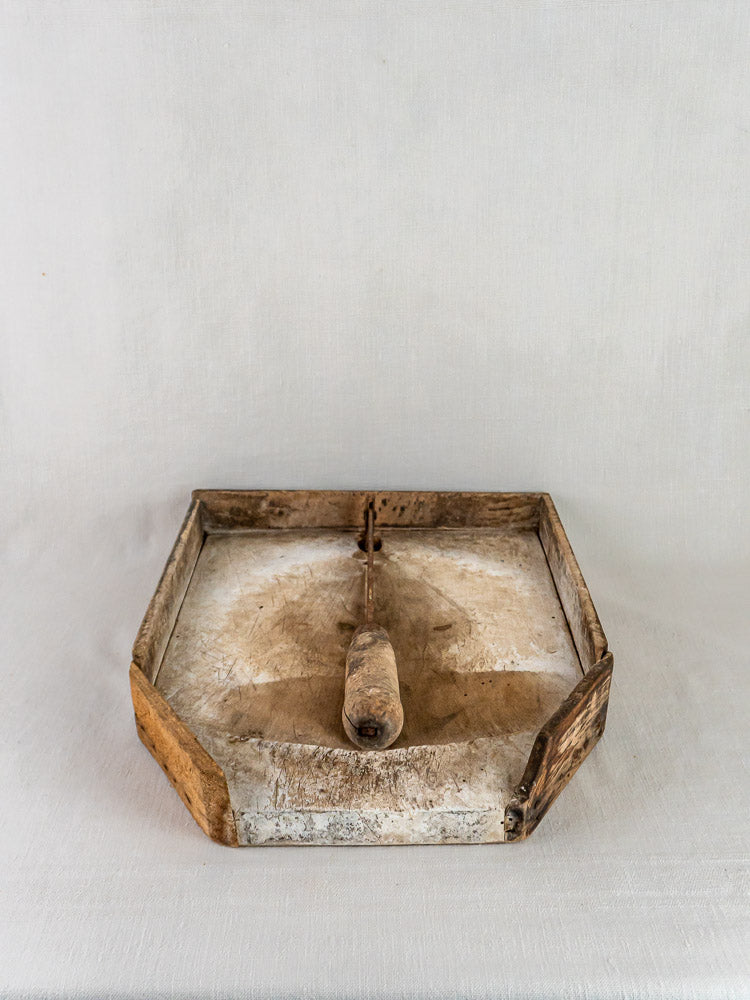 Antique French wood and iron tobacco cutter with weathered handle on neutral surface, plain backdrop.
