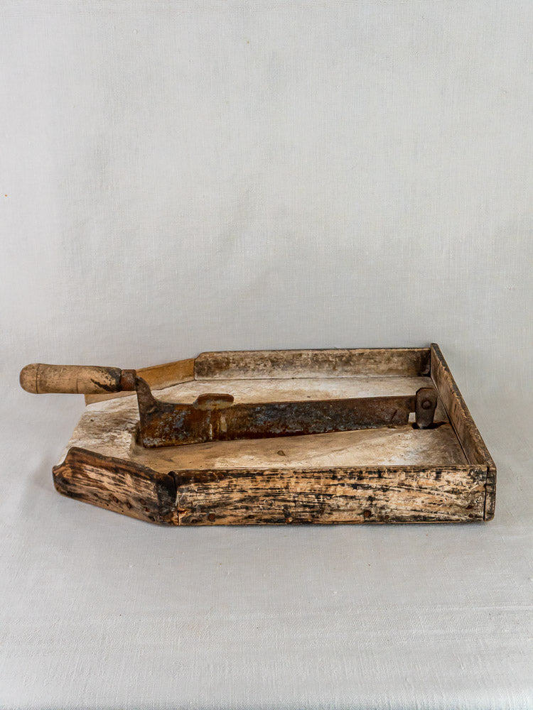 Antique French wood and iron tobacco cutter with curved blade on a light surface, plain background.