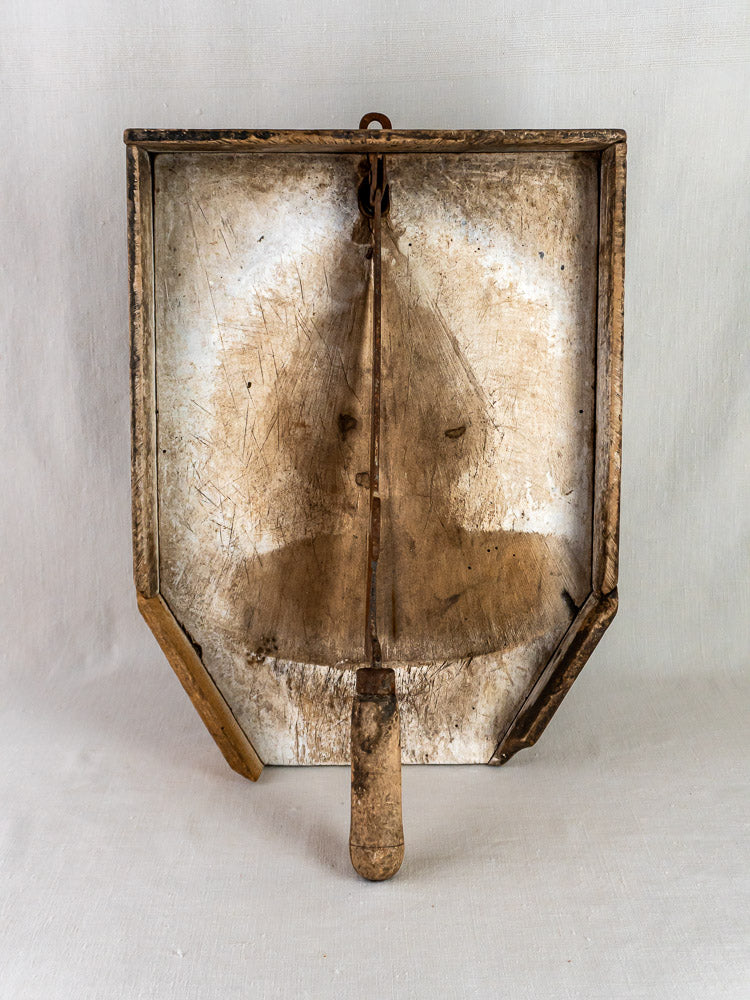 A vintage metal dustpan with patina and stains, evoking antique French tobacco cutter motifs.