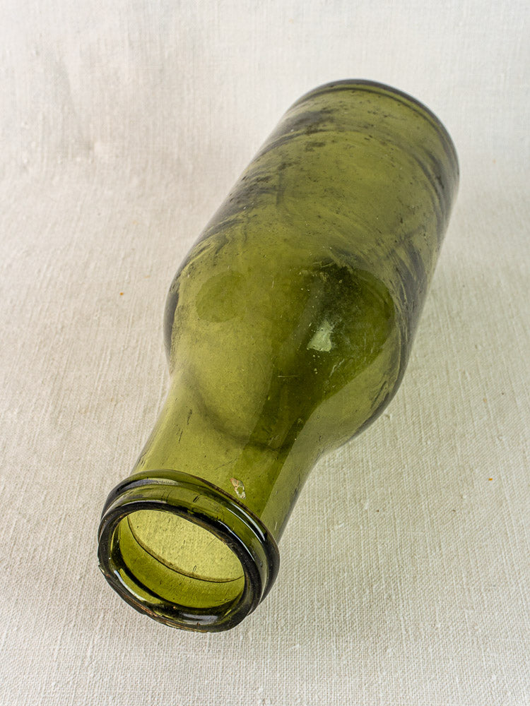 Antique French truffle bottle, 19th-century hand blown olive glass, resting on light fabric.