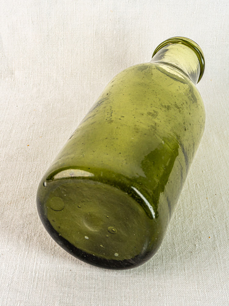 Antique French olive glass truffle bottle with reflective surface on light textured fabric.