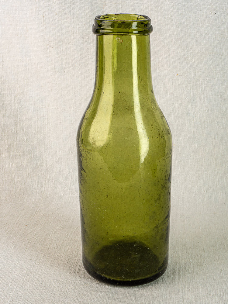 Antique French olive green glass truffle bottle with short neck on textured surface, light background.