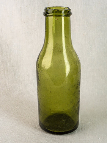 Antique French olive green glass truffle bottle with short neck on textured surface, light background.
