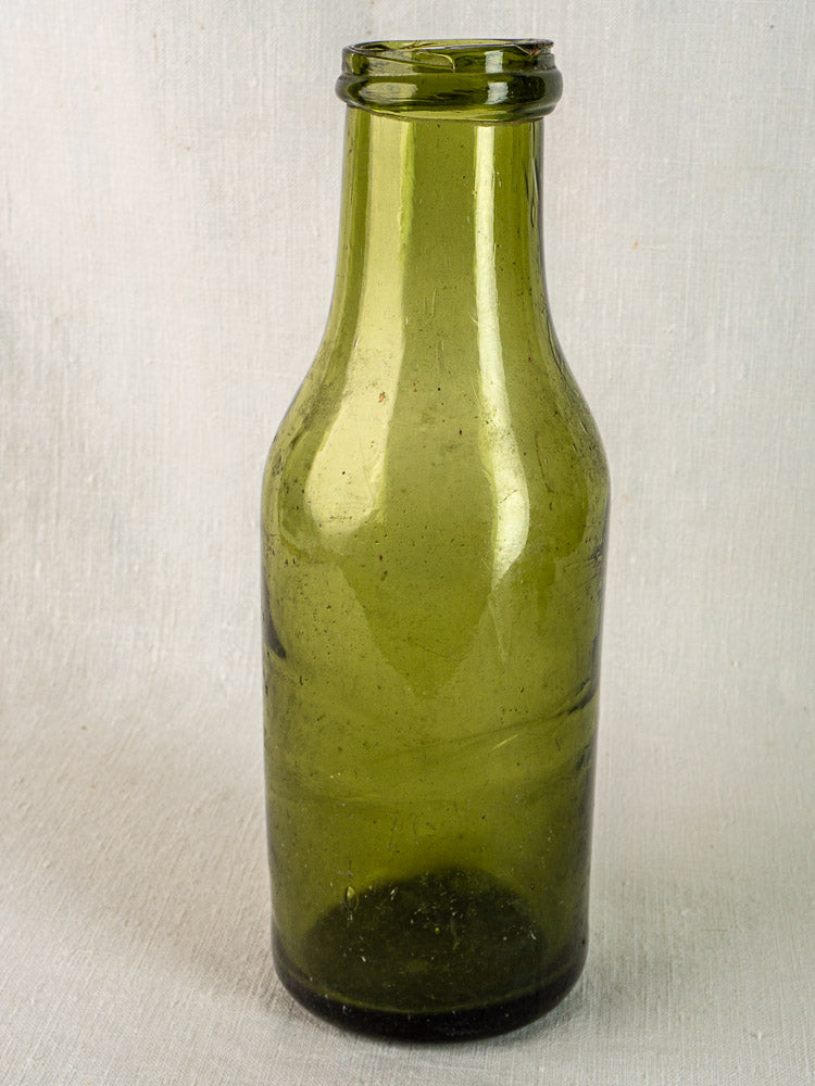 Hand blown 19th-century French olive glass truffle bottle with narrow neck, no label, on plain background.