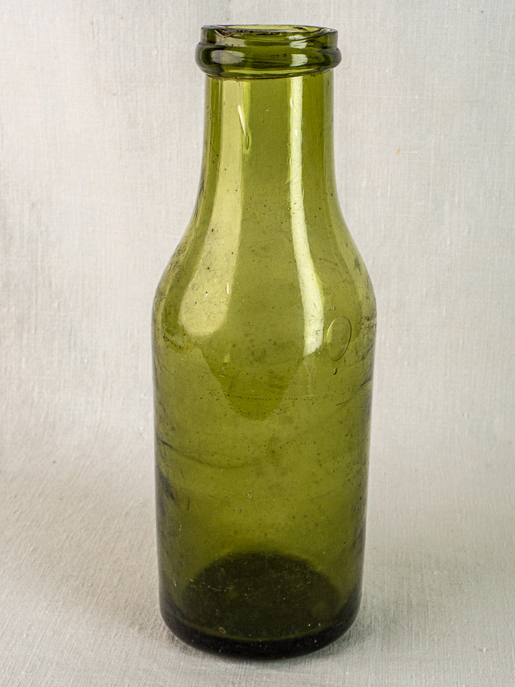 Antique French hand-blown olive glass truffle bottle with short neck on textured surface.