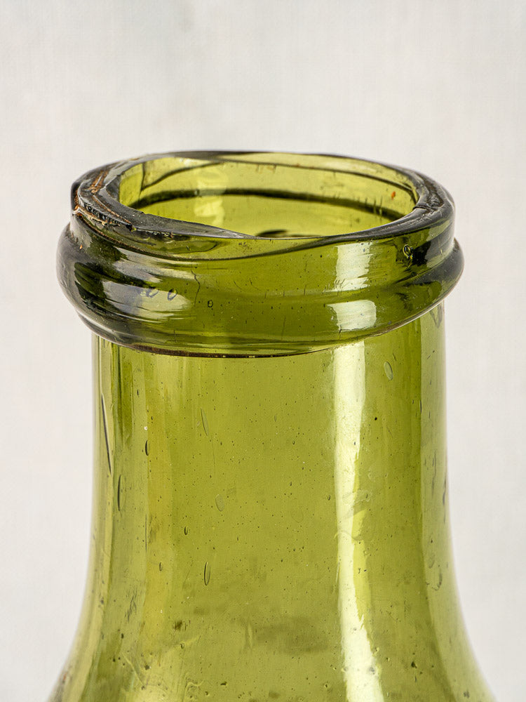 Close-up of antique French truffle bottle neck in hand-blown olive glass with jagged rim.