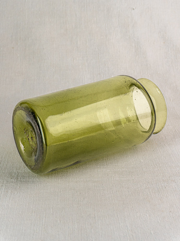 Antique French hand-blown olive green glass preserve jar with wide mouth on light gray textured surface.