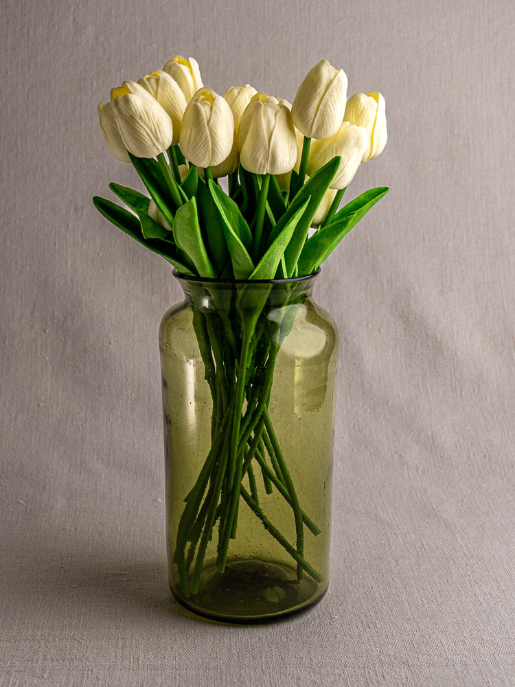 Antique French hand-blown olive green glass preserve jar with white tulips, late 18th century, on gray fabric.